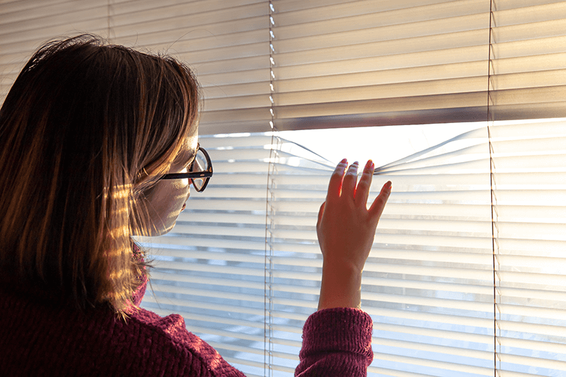 Woman opening blinds to look outside.